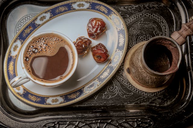 A beautifully served cup of authentic Turkish coffee with a thick foam, alongside a glass of water and Turkish Delight.